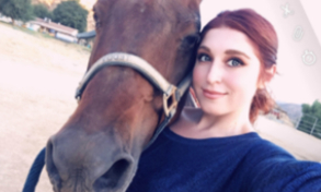 A woman standing next to a horse on the ground.