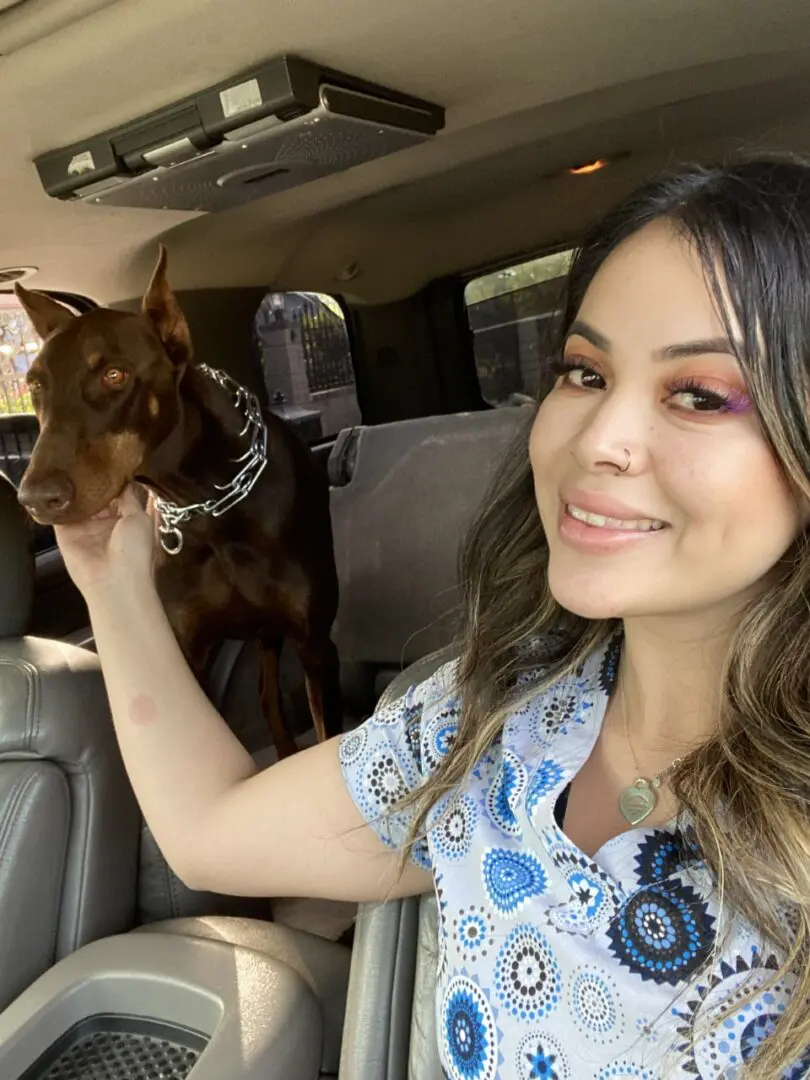 A woman sitting in the back of a car with her dog.